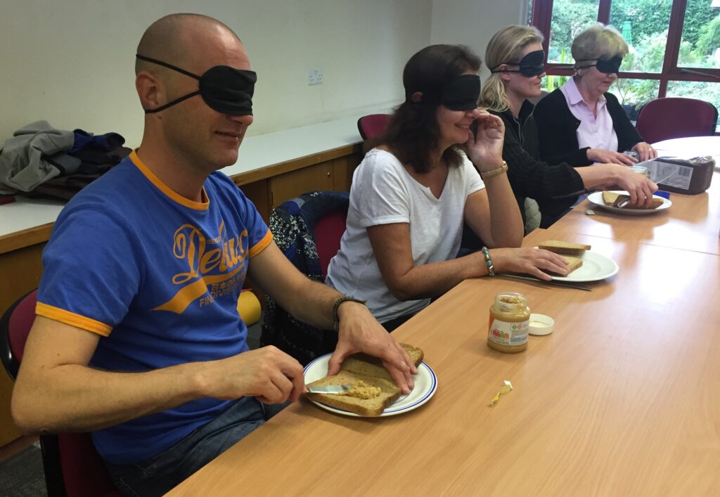 4 individuals with blindfolds trying to make sandwiches on a training course. 
