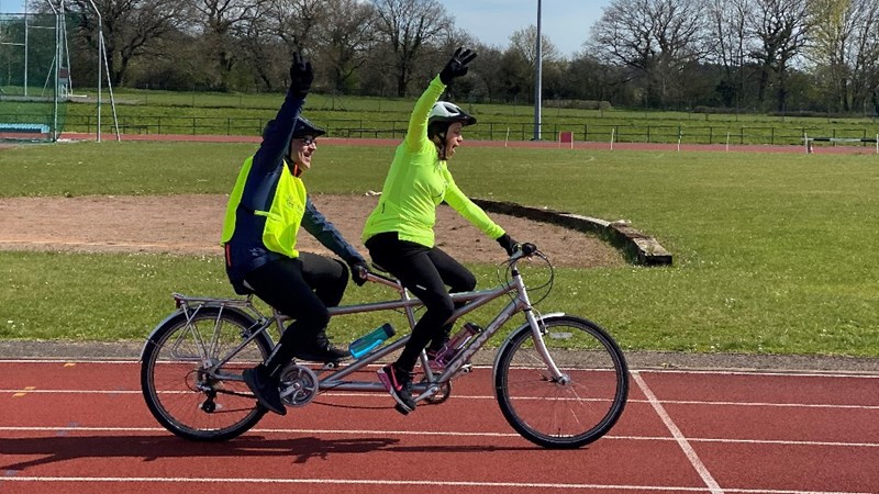 Two people riding a tandem at Horspath with their fists in the air