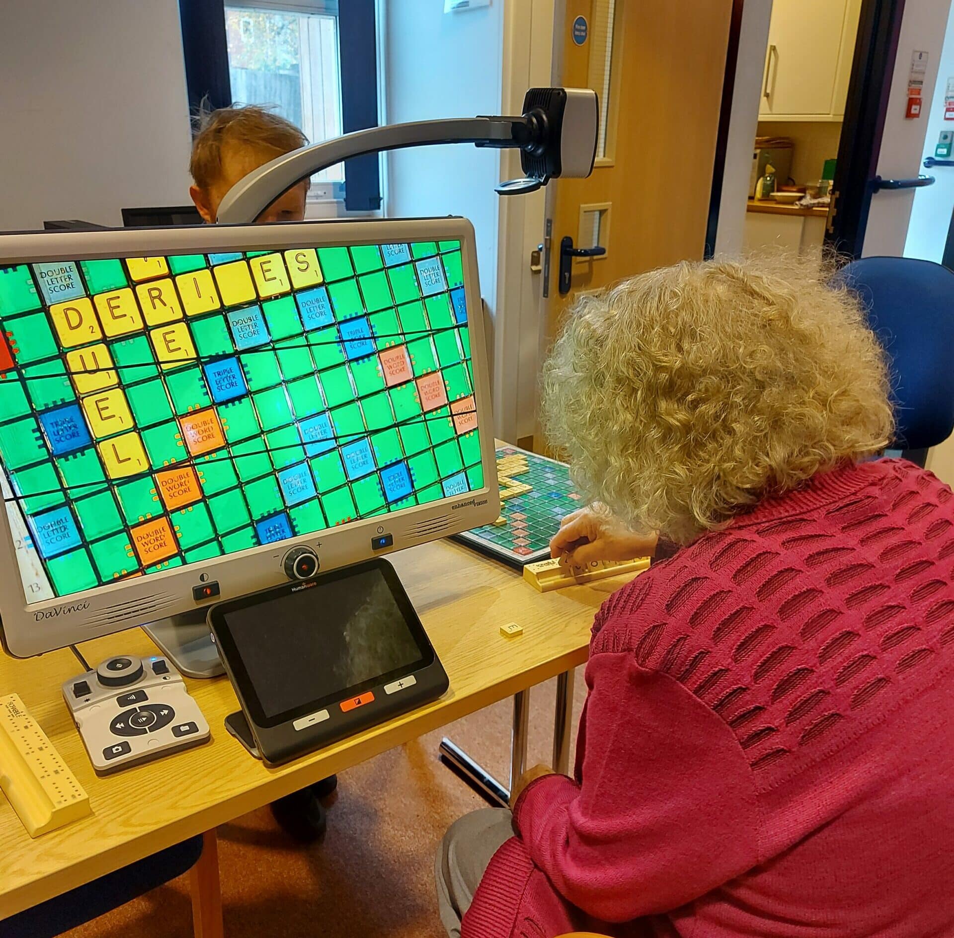 A photo of one of our clients from behind, using a CCTV magnifier to play Scrabble.