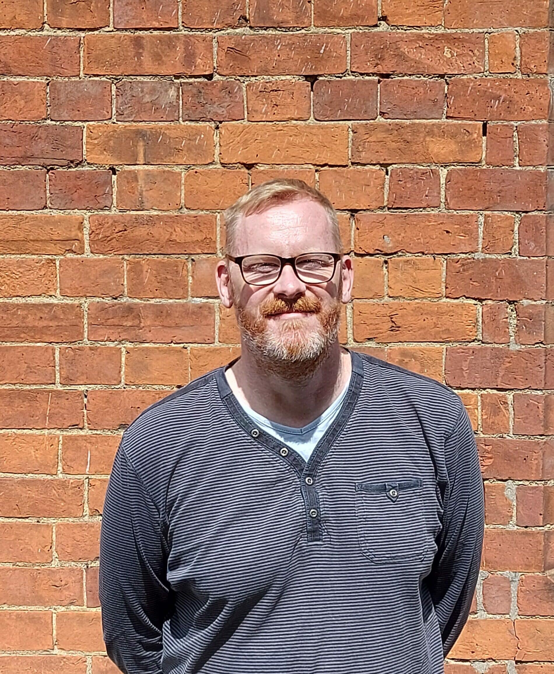 A photo of Andy, smiling in front of a brick wall