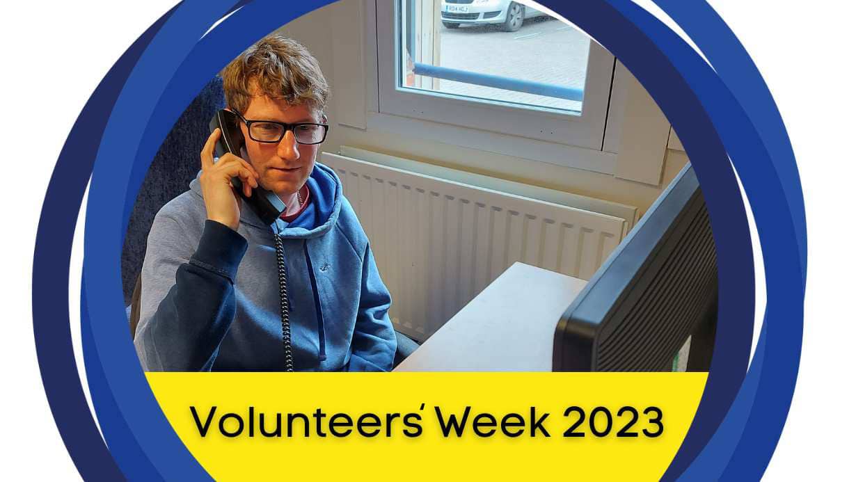 A photo of Mike talking on the phone. There is a yellow banner below that says, 'Volunteers' Week 2023.'