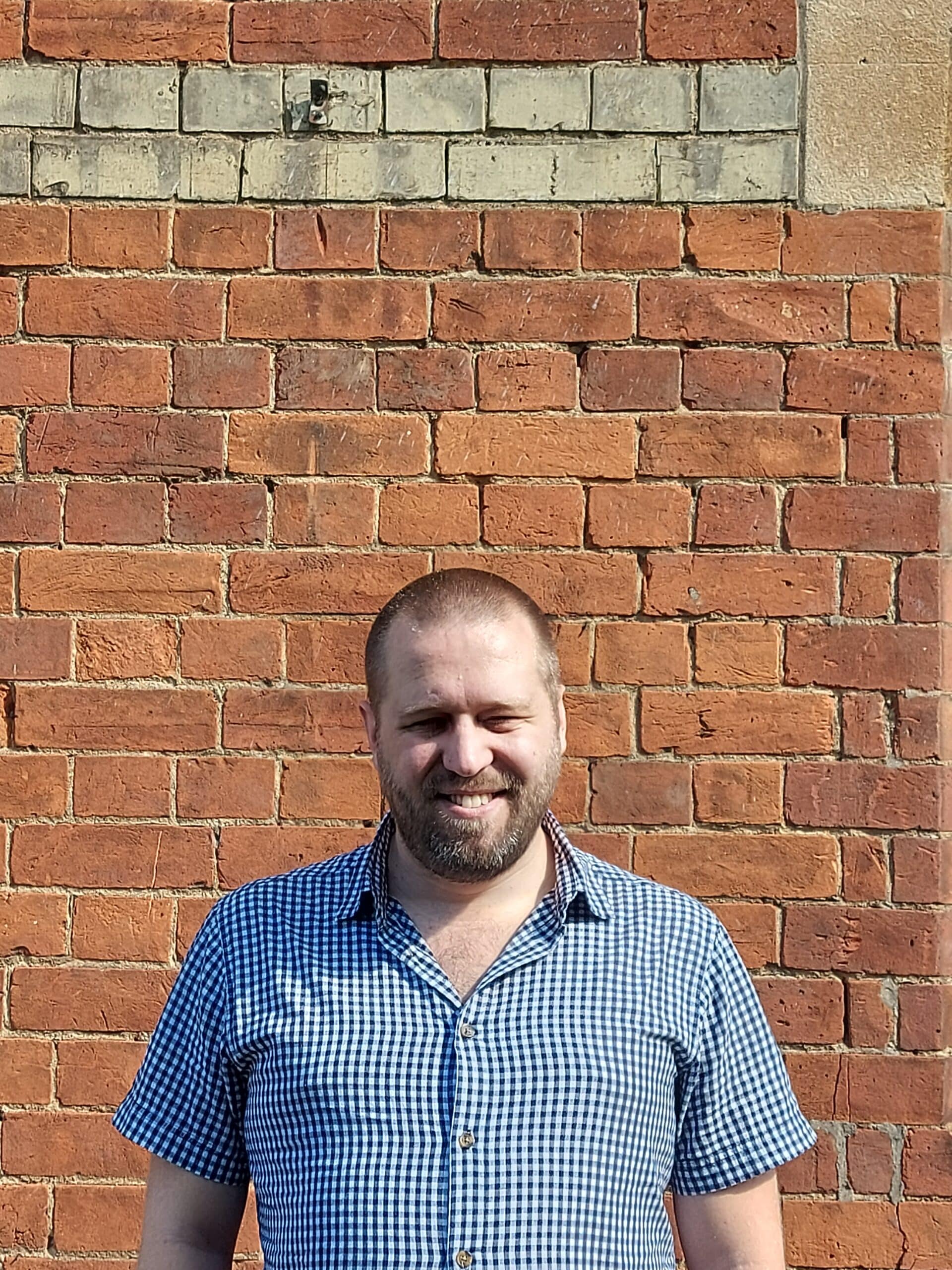 Andreas posing for a photo and smiling in front of a brick wall