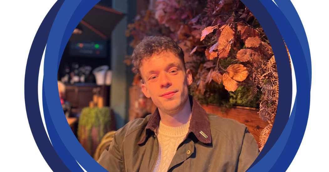 Jamie sitting in front of a flower wall and posing for a photo