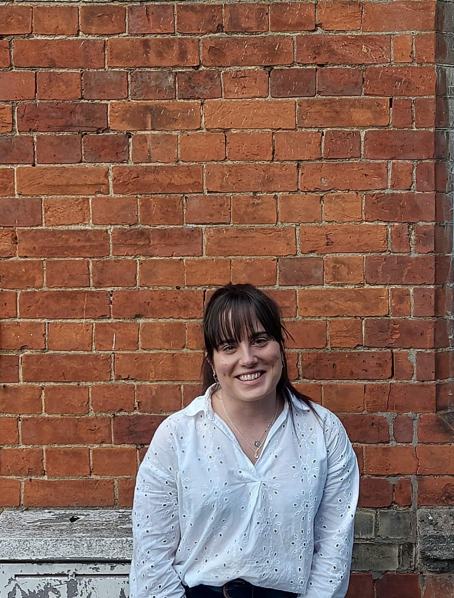 Katie smiling and posing in front of a brick wall.