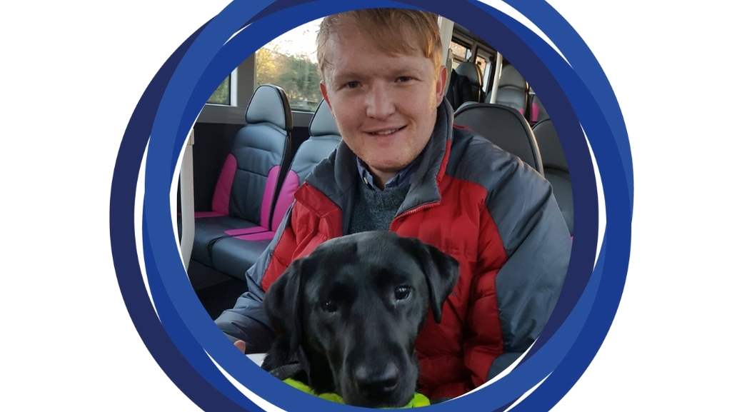 Nathan sitting on a bus and smiling with his guide dog, Maisie